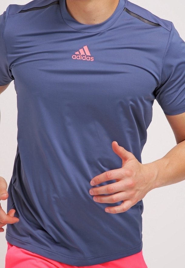 Camiseta deportiva azul de material ligero con mangas cortas, con detalles en negro en los hombros y un logo rosa de Adidas en el pecho.