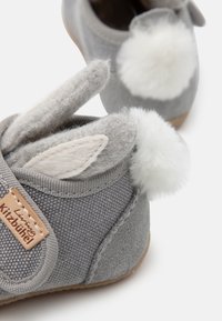 Pilki audiniai šlepetės su minkšta tekstūra, su triušio ausų akcentais ir pūkuota balta pom-pom galinėje pusėje. Lengvas padas ir siuvinėtos detalės.