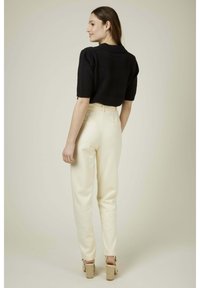 Pull noir court avec des manches courtes associé à un pantalon taille haute de couleur crème avec une texture lisse et des poches arrière.