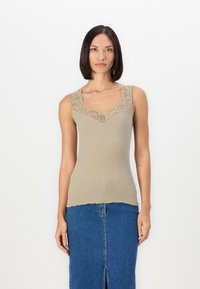 Beige ribbad toppi med V-hals og blomsterlakt kant. Bølgeformet kant. Kombinert med en denimskjørt med en frontslipp.