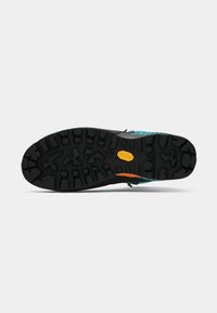 Sola de Vibram preta com sulcos profundos em um sapato de caminhada turquesa e laranja contra fundo branco.