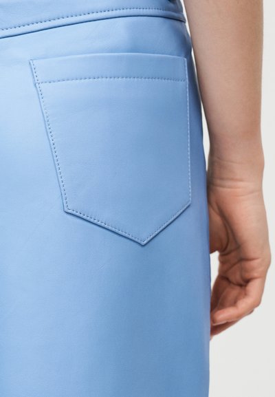 Κοντινό πλάνο μιας ανοιχτό μπλε δερμάτινης φούστας που δείχνει μια ραμμένη πίσω τσέπη και το χέρι ενός ατόμου χαλαρά στο πλάι του.