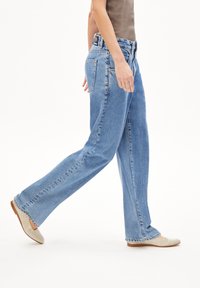Light blue denim jeans with a loose fit, five pockets, and visible stitching details. Pair of beige flat shoes completes the look.