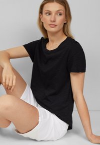 Zwarte T-shirt met korte mouwen, zachte textuur, ronde halslijn en een relaxte pasvorm, gecombineerd met witte shorts. Eenvoudig en veelzijdig ontwerp.