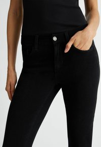 Jeans in denim nero con una vestibilità slim, caratterizzati da una chiusura frontale a bottone, cinque tasche e una texture liscia. Vita media.