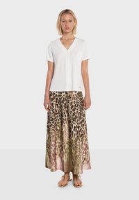 Haut blanc à manches courtes avec un col en V, associé à une longue jupe plissée arborant un motif léopard marron et beige. Tongs dorées.