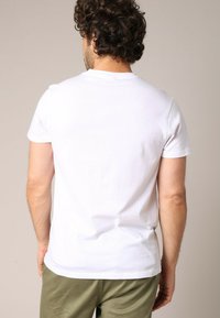 T-shirt en coton blanc à manches courtes, avec un col rond et une texture lisse. Présenté sur un modèle masculin, vu de dos.