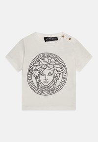 Krémové bavlněné tričko s černou grafikou Medusy a kruhovým vzorem řeckého klíče. Obsahuje zlaté knoflíky na jednom rameni.