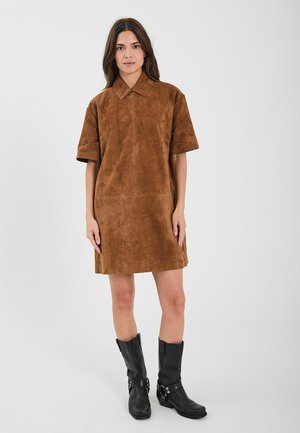 Brown suede shirt dress with short sleeves and a pointed collar, featuring a front zipper. Paired with black ankle boots.
