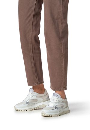 White and silver sneakers with mesh and synthetic material, textured sole, and unique design elements. Worn with brown cropped pants.