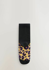 Svart strumpa med ett leopardmönster på en gul bakgrund, texturerad stickad tyg, med längd till mitten av vaden och med solid svart topp.