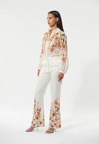 White floral blouse with a collar and gathered sleeves paired with white pants featuring floral embroidery at the hems. Silver sandals.