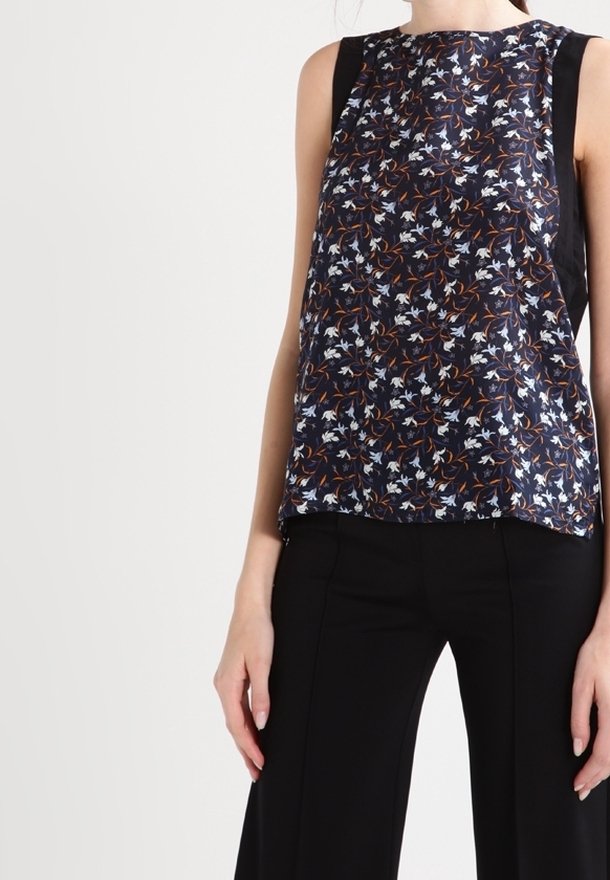 Blouse sans manches bleu marine avec imprimé floral en blanc et orange. Présente des panneaux latéraux noirs et une coupe décontractée. Tissu lisse et léger.