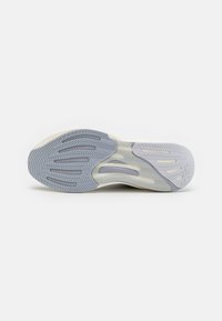 Semelle de chaussure avec un motif en caoutchouc texturé gris et blanc, présentant des rainures et des crêtes pour une adhérence et un soutien.