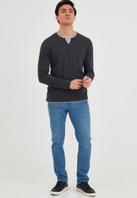 Langærmet, mørkegrå T-shirt med V-hals og kontrastfyldt lysgrå indvendig krave. Sammen med lyseblå jeans og sorte sneakers.