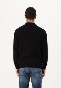 Svart stickad tröja med krage, långa ärmar och en slät textur. Kombinerad med urtvättade blå jeans med sömmar på bakfickorna.