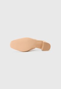 Nude hoge hak met een ronde neus, glad synthetisch materiaal en een textuur in de zool. Vierkante blokhak voor stabiliteit.