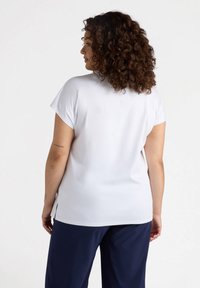 Top blanco de manga corta con un ajuste relajado, que presenta aberturas laterales y una textura suave. Combinado con pantalones azul marino, mostrando un diseño minimalista.