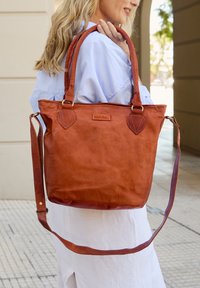 Borsa tote in pelle marrone con doppio manico, tracolla regolabile e dettagli cuciti. Presenta una forma rettangolare e una superficie testurizzata.
