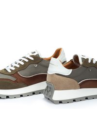 Scarpe sportive con una combinazione di tessuto verde oliva, dettagli in suede marrone, suola in gomma grigia e lacci bianchi, con un particolare dettaglio testurizzato sul tallone.