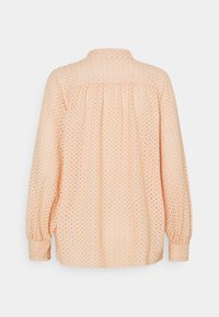 Blouse à manches longues couleur pêche claire en tissu brodé avec un détail de plissé sur l'empiècement, vue de dos sur un fond uni.