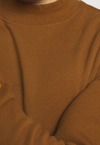 Brun stickad polotröja med en mjuk textur, smal passform och subtila sömdetaljer. Tyget verkar sträckt och bekvämt.