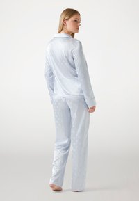 Ensemble de pyjama en satin bleu clair comprenant une chemise à col à manches longues et un pantalon assorti, avec un motif subtil et une texture lisse.