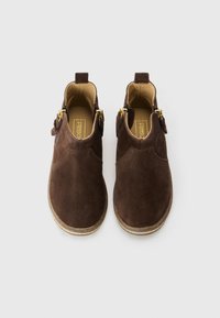 Botas de tobillo de ante marrón con cremalleras doradas y una suela texturizada. Cuentan con una punta redondeada y un tacón pequeño para mayor estabilidad.