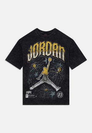 T-shirt noir avec un grand texte jaune et blanc "JORDAN", une silhouette de joueur de basket tenant un ballon, toiles d’araignée et araignées en motif graphique.