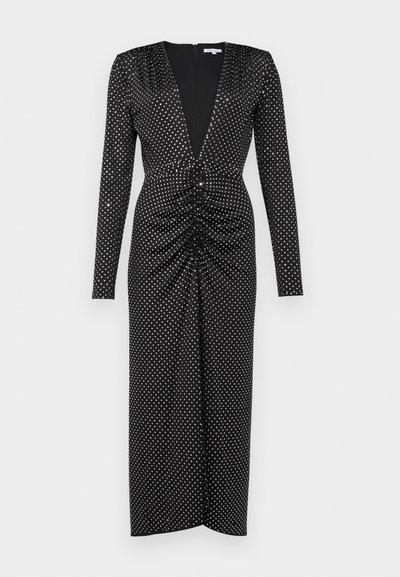 Lange zwarte jurk met een diepe V-hals, lange mouwen, gerimpelde details bij de taille en een zilveren stippenpatroon over de hele jurk.