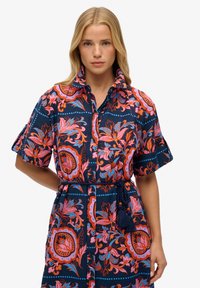 Robe à manches courtes en coton bleu marine ornée de motifs floraux vibrants en rose, orange et bleu, avec une ceinture nouée et une fermeture à boutons.