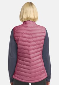 Gilet puffo rosa con trapuntatura a chevron, colletto alto e texture liscia; indossato sopra una maglietta a maniche lunghe scura e testurizzata.