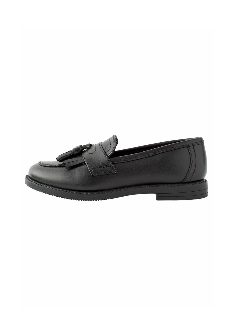 Mocasín de cuero negro con punta redondeada, acentos decorativos de borlas y suela plana de goma. Presenta costuras a lo largo del empeine.
