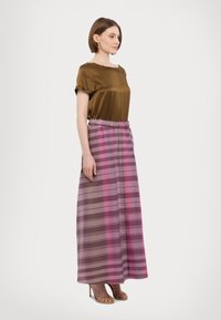 Top in raso marrone con maniche corte abbinato a una lunga gonna a quadri in tonalità di rosa e viola, dotata di un elastico in vita.