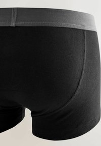 Primer plano de bóxers ajustados negros con una cintura elástica gris, mostrados desde atrás sobre un fondo claro.