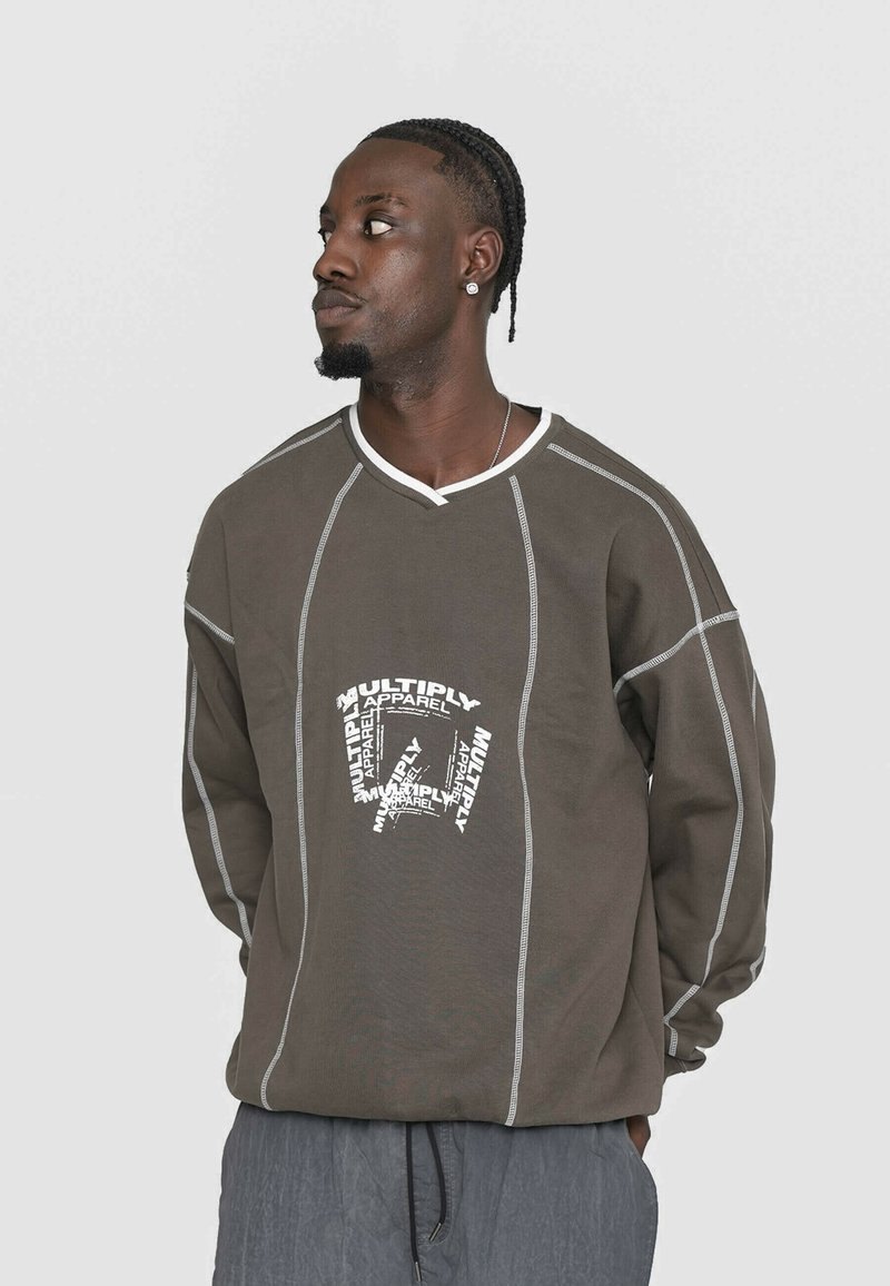 Hnedá mikina so bielym kontrastným prešívaním a grafickým potlačou s nápisom "MULTIPLY APPAREL." Má výstrih do V a voľný strih.