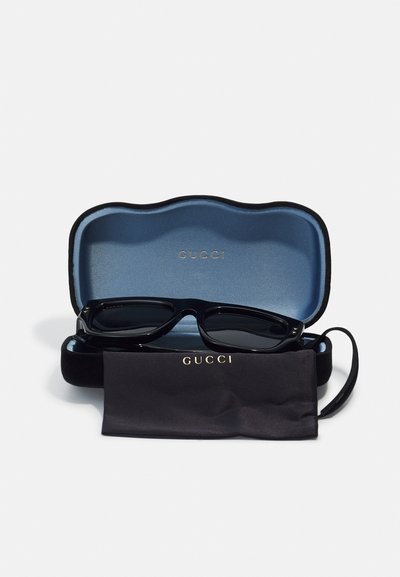 Occhiali da sole Gucci in una custodia nera con interno azzurro chiaro. Include un panno per la pulizia nero, il tutto con dettagli del logo dorato.
