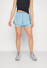 Vaaleansiniset urheilushortsit, joissa on kerroksittainen design ja sisäänrakennettu sisäshortsi. Kuminauhavyötärö, Nike-logo vasemmalla edessä.