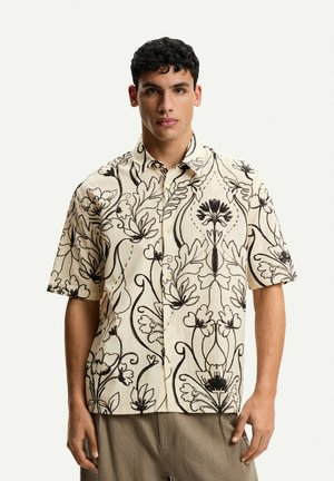 Camicia a maniche corte realizzata in tessuto leggero, con uno sfondo beige e intricate fantasie floreali nere, dotata di chiusura con bottoni.
