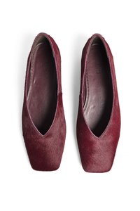 Ballerines bordeaux en matériau doux et texturé, avec un bout pointu et une ouverture en forme de V. Intérieur en cuir lisse et détails de couture subtils.