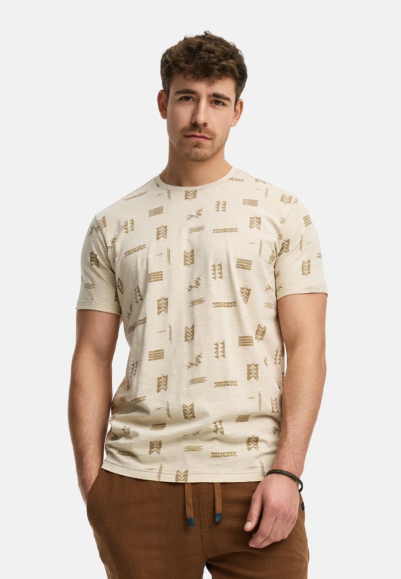 T-shirt beige à manches courtes avec un motif de formes et de lignes abstraites brunes. Texture douce, col rond et coupe standard.