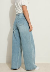 Jeans de pernera ancha de color azul claro con una cintura alta, confeccionados en denim. Cuentan con dos bolsillos traseros y un ajuste holgado. Suave al tacto y con un acabado limpio.