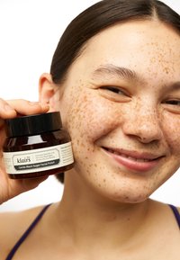 Klairs Gentle Black Sugar Facial Polish i en mörk burk med svart lock. Etiketten är krämfärgad med svart text. Modellen har en slät hy med fräknar.