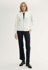 Hoodie blanche zippée avec une coupe décontractée et des poignets côtelés, associée à un jean droit en denim bleu foncé et des bottines noires.