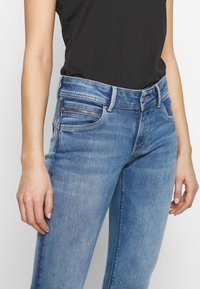 Ljusblå denimjeans med smal passform, lätt urtvättad textur, fem fickor och en dragkedjeficka framtill.