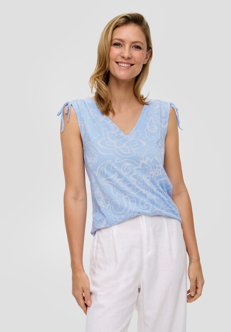 Lichtblauw mouwloos topje met een V-hals en bloemenpatroon, voorzien van verstelbare strikjes op de schouders, gecombineerd met witte linnen broek.