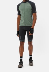 Męski strój rowerowy składający się z zielonej koszulki z krótkim rękawem na zamek, czarnych akcentów oraz dopasowanych czarnych spodenek z geometrycznym wzorem.