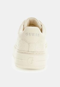 Sneaker color crema con un motivo testurizzato, logo in rilievo sul tallone e una suola bianca spessa con accenti sottili.