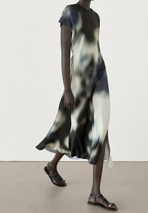 Personne à la peau foncée marchant dans une robe fluide à manches courtes avec un motif abstrait en noir, blanc et gris, et des sandales plates noires.