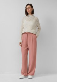 Crème gebreide trui met een golvende textuur, gecombineerd met lichtroze hooggetailleerde broek. Witte sneakers maken de look compleet.